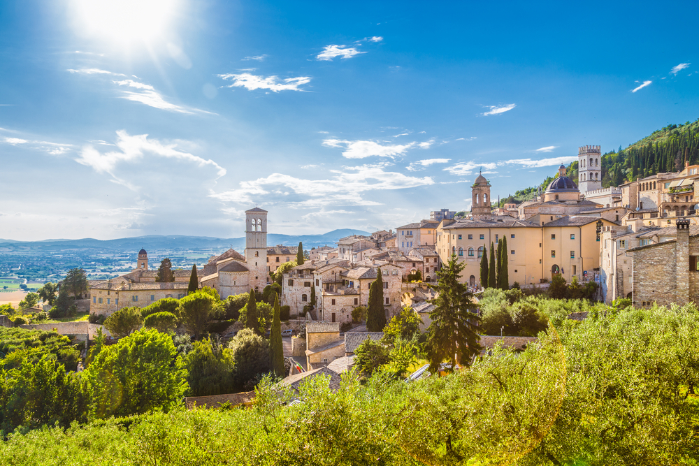 Panoramic view of the historic town of Assisi in beautiful golden morning light at sunrise on a sunny day with blue sky and clouds in summer, Umbria, Italy
