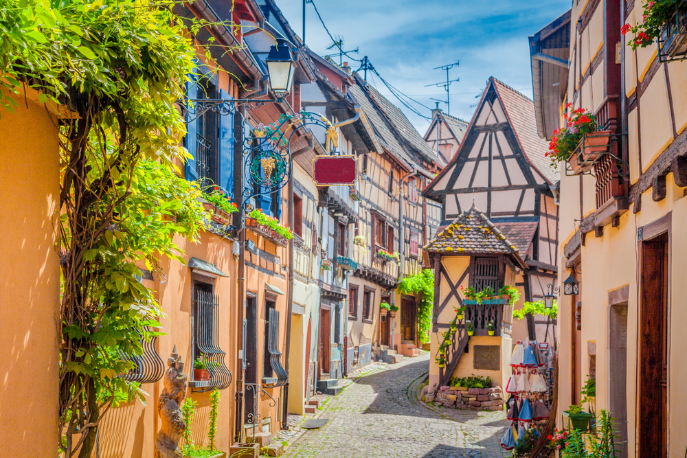 Beautiful view of charming street scene with colorful houses in the historic town of Eguisheim on an idyllic sunny day with blue sky and clouds in summer, Alsace, France