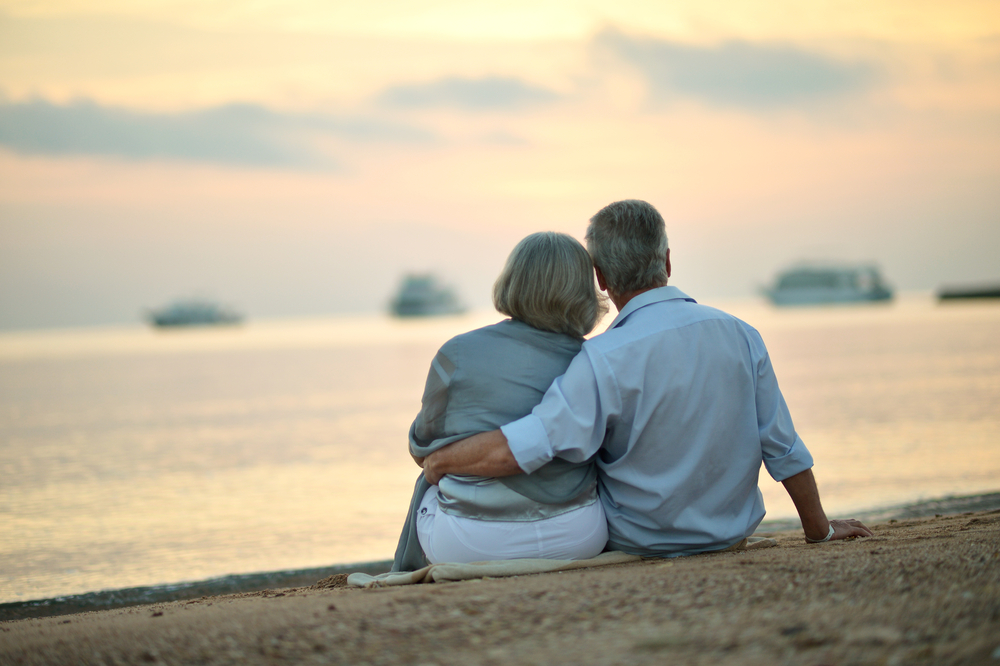 Happy Mature couple relaxing on beach at sunset,back view