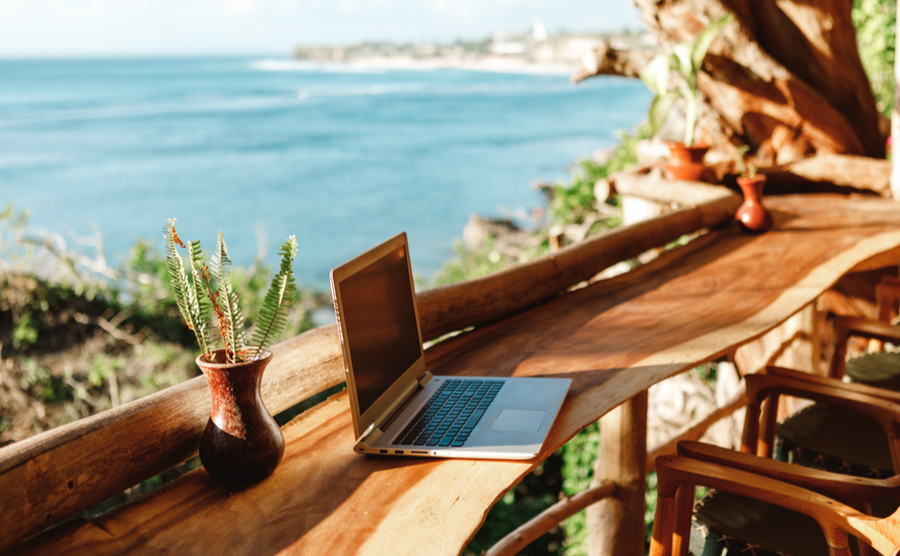 Open laptop with black screen on wooden table work space outdoors with amazing view on the ocean. Laptop on sea view backdrop