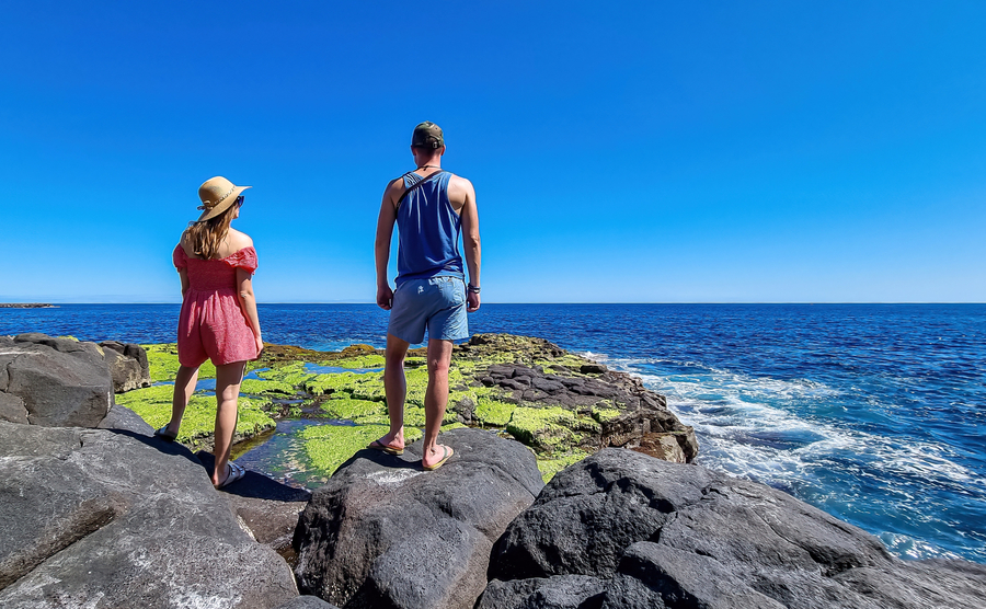 Couple with scenic view on volcanic rocks overgrown by moss, green sea plants, algae on coastline in Puerto de la Cruz, Tenerife, Canary Islands, Spain, Europe. Ocean bath Laja de la Sal. Wave hitting