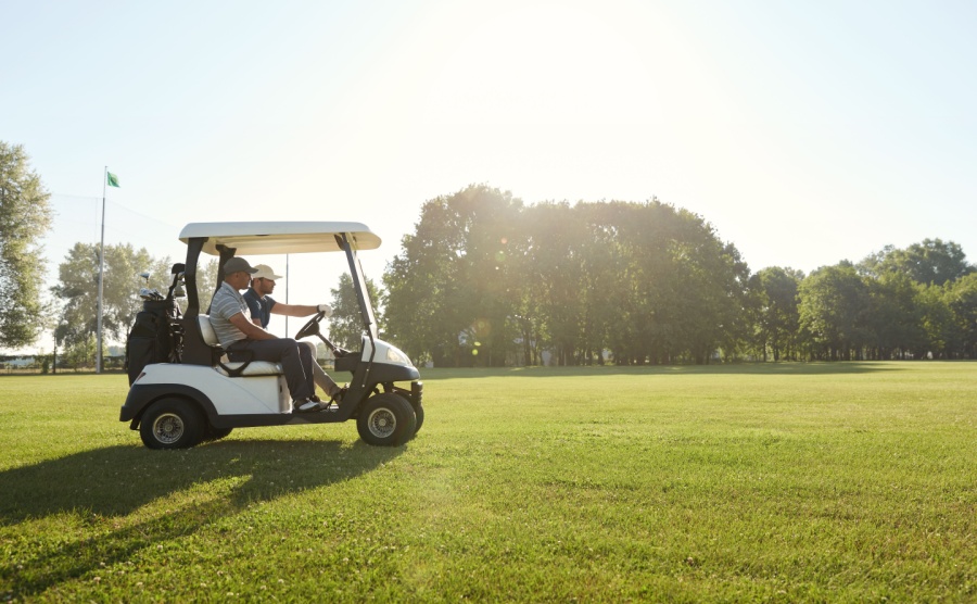 Side view of golfers riding golf cart on green lawn of golf field at warm sunny day. 